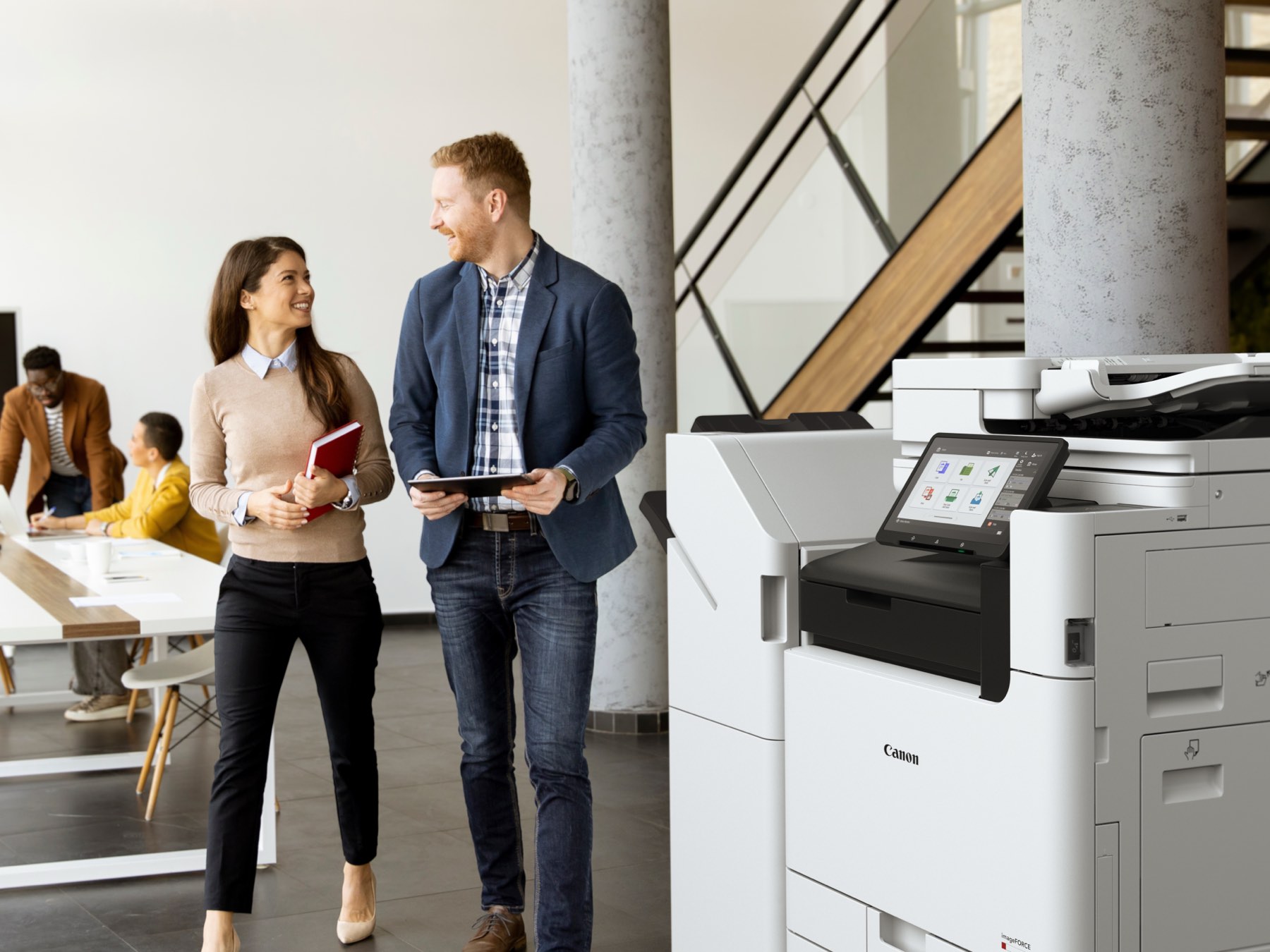 Two colleagues walk past a Canon imageFORCE multifunction printer in a bright, modern office